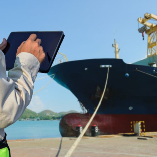 Workers in shipyard hand holding tablet check condition for ship repair by front ship in shipyard background